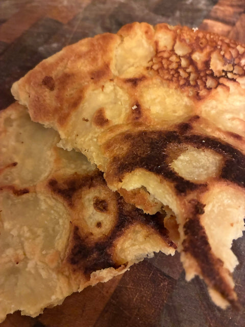 Cecina Toscana, a golden chickpea flour pancake with browned spots, torn open on a wooden board